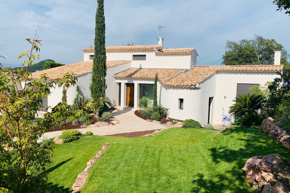 A white house with a tiled roof is surrounded by a lush green lawn