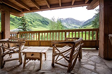 A balcony with chairs and a table with mountains in the background
