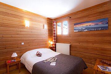 A cozy, wood-paneled bedroom with a bed, mountain views from the window, and a panoramic winter scene artwork creating a rustic, warm ambiance.