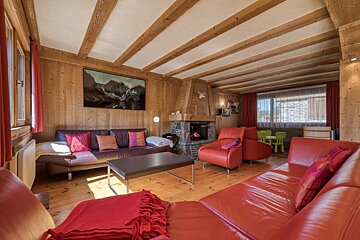 Cozy chalet living room featuring wood-paneled walls, exposed ceiling beams, red leather sofas, and a stone fireplace.