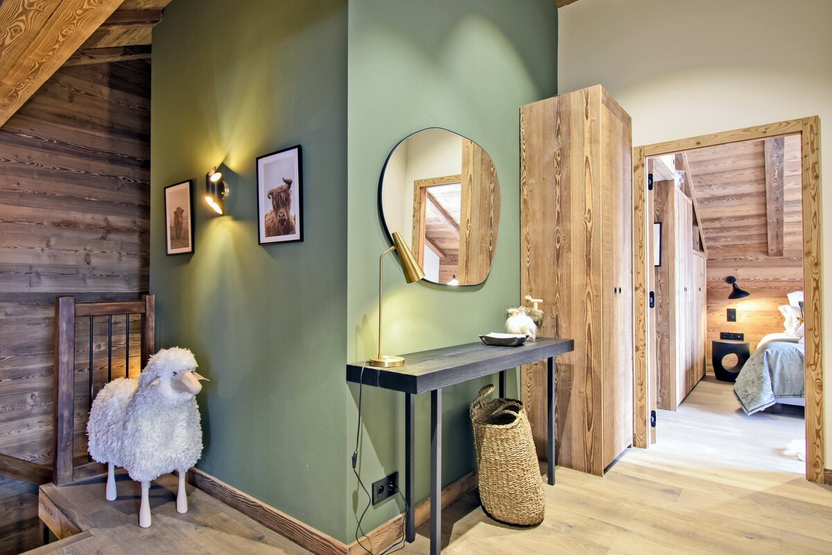 Cozy chalet hallway with a green wall, wooden accents, a console table with a mirror, and a decorative sheep.