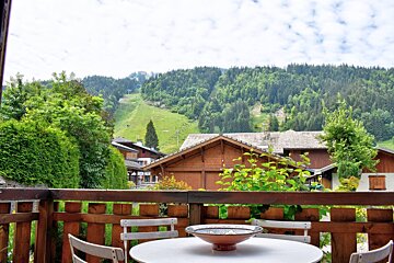 View from a wooden balcony with a table and chairs overlooking chalets and a lush, tree-covered mountain.