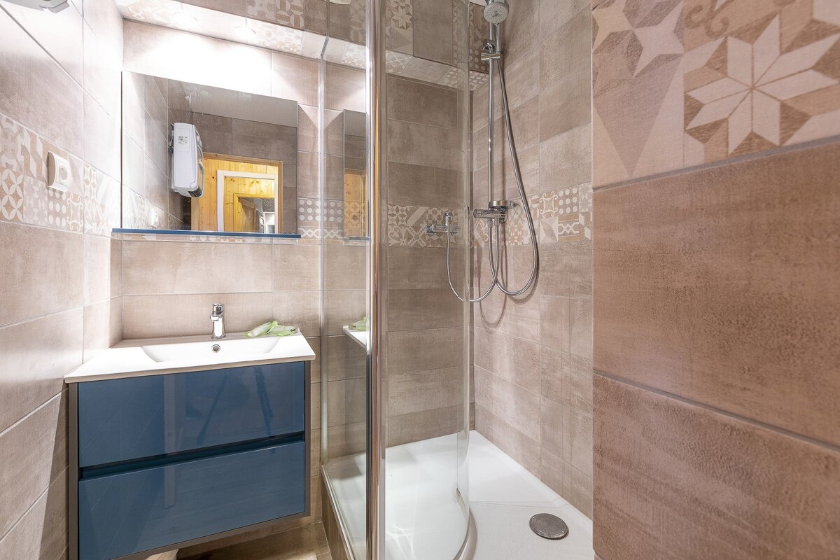 Modern bathroom with a blue vanity, mirror, and tiled shower stall. Beige and brown patterned tiles adorn the walls.