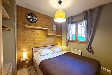 Cozy bedroom featuring a double bed, wood-paneled accent wall, hanging lamp, and a window with grey curtains.