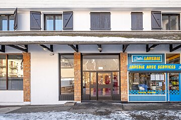A white building facade with dark-shuttered windows and snow on the roof ledge and ground. A