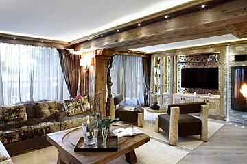 Rustic-chic chalet living room featuring warm wood walls/ceiling, fireplace, TV, plush seating, and champagne on a wooden coffee table.