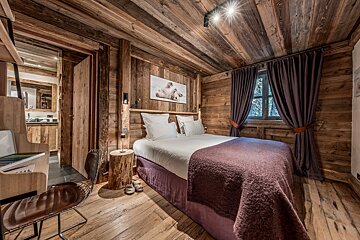 Cozy chalet-style bedroom with rich wooden paneling, a bed with a purple throw, window, polar bear art, and a peek into the bathroom.
