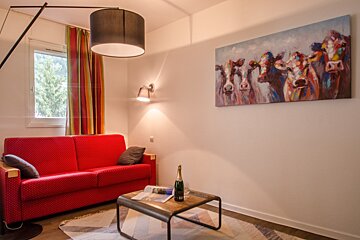 A living room with a red couch and a painting of cows on the wall