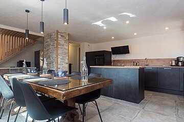Modern open kitchen and dining room featuring a wooden table with black chairs, dark cabinets, and a stone-clad wall accent.