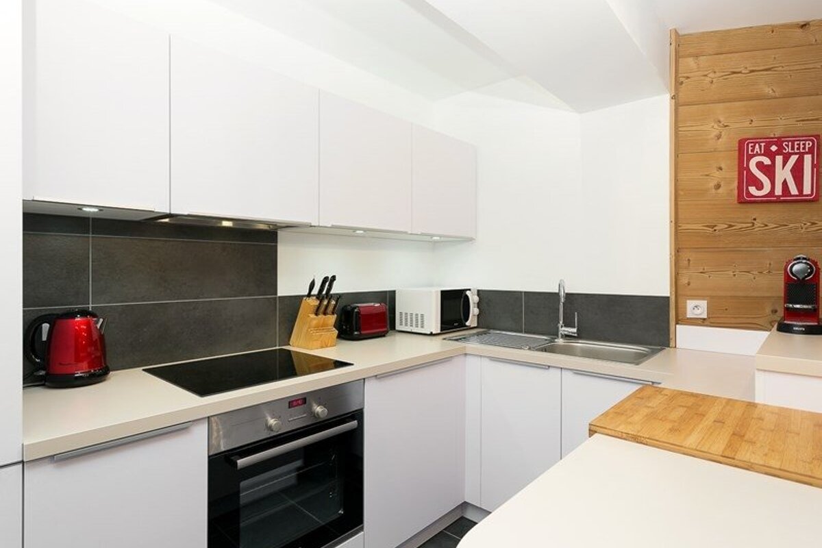 Modern kitchen with white cabinets, dark backsplash, red appliances, and a wood-paneled wall featuring an "EAT SLEEP SKI" sign.