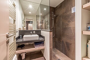 A modern bathroom with a white vessel sink, large mirror, and a glass-enclosed shower with dark stone tiles.