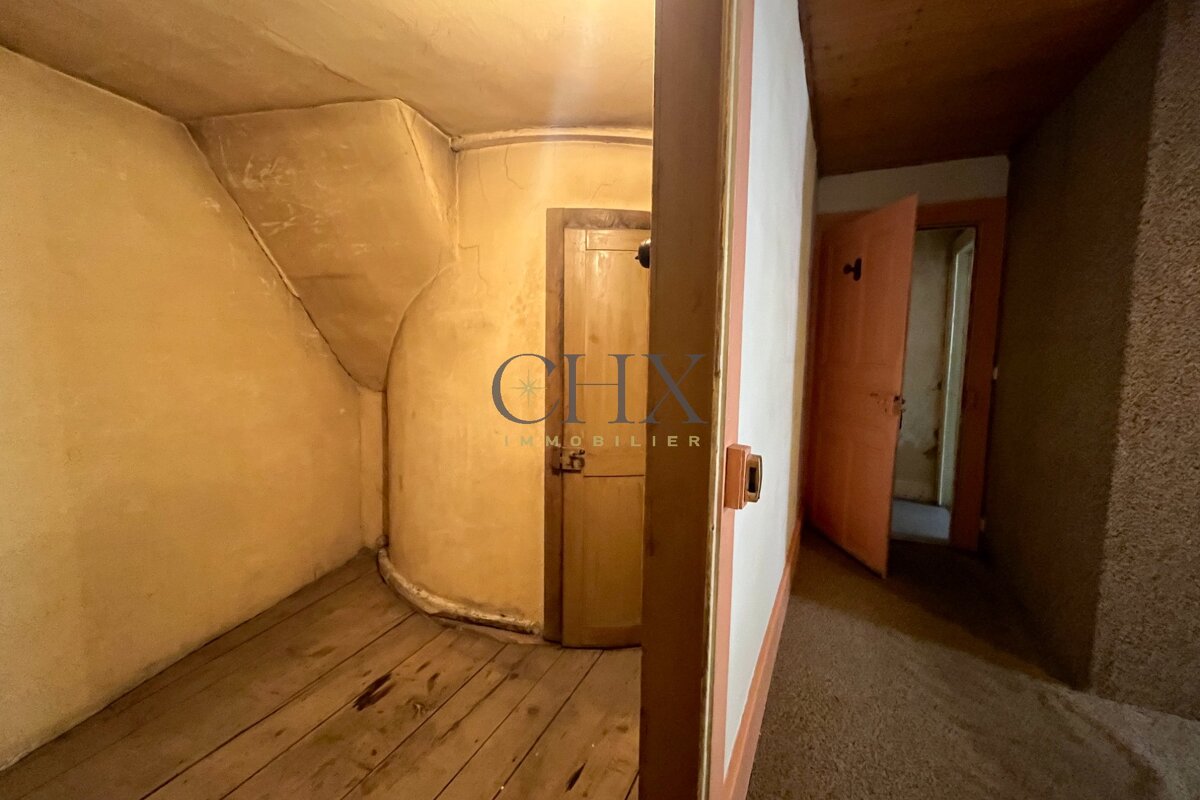 Rustic interior showing an old room with curved plaster walls, wooden floors, and a hallway with an open door.