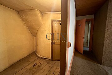 Rustic interior showing an old room with curved plaster walls, wooden floors, and a hallway with an open door.