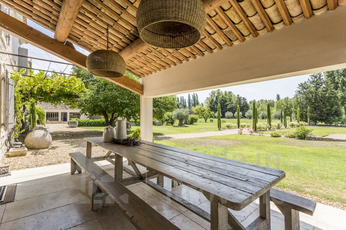 A large wooden picnic table is under a covered patio