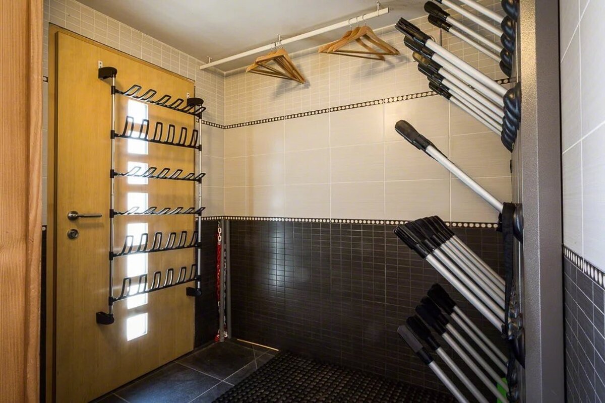 A ski storage room with racks for boots and skis, wooden hangers, and tiled walls.