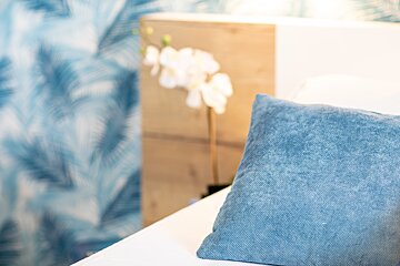 A blue pillow sits on a bed next to a plant