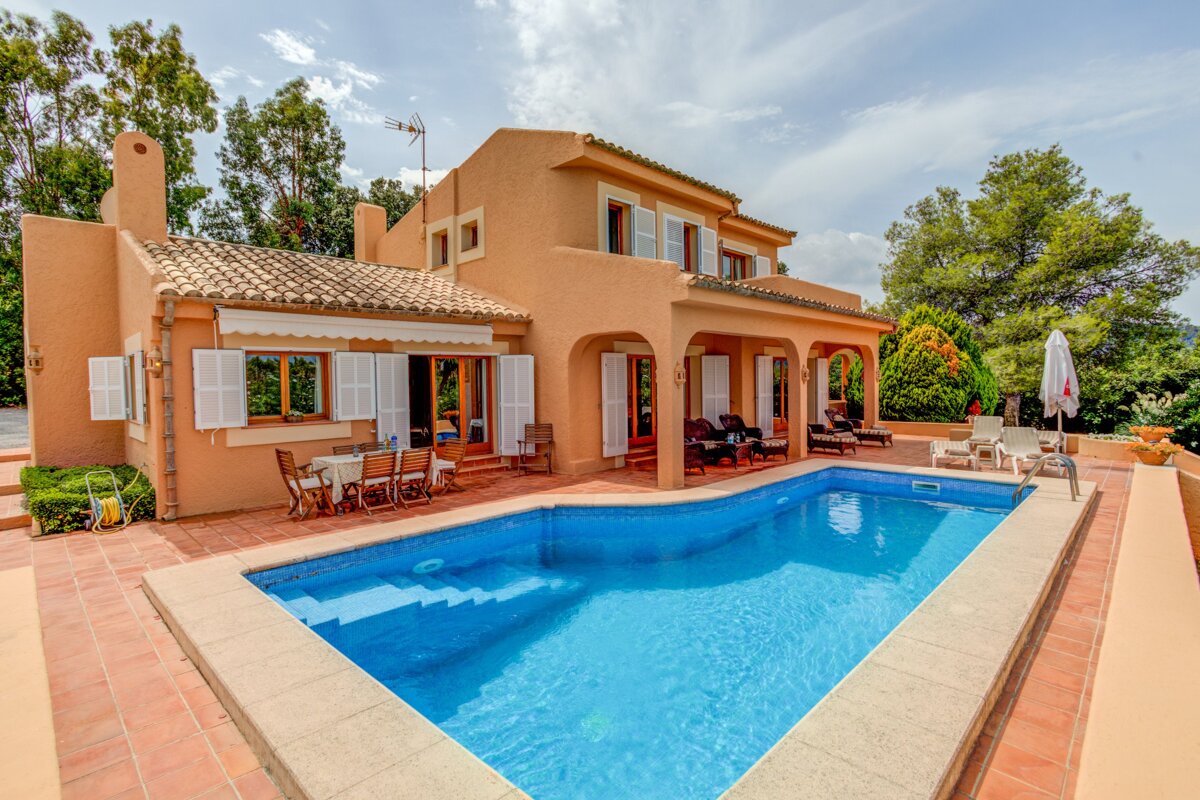 A charming orange villa with a sparkling blue pool, tiled patio, and lush green trees under a sunny sky, ideal for relaxation.