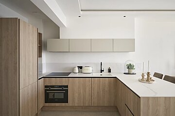A modern, minimalist kitchen with light wood cabinetry, white countertops, and sleek built-in appliances under soft lighting.