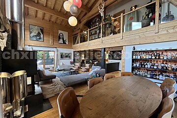 A grand, rustic-modern chalet interior featuring wood paneling, a dining area, cozy lounge, mezzanine, and a large liquor display.
