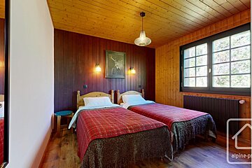 Rustic bedroom with two single beds, wood paneling on walls and ceiling, a framed deer portrait, and a large window.