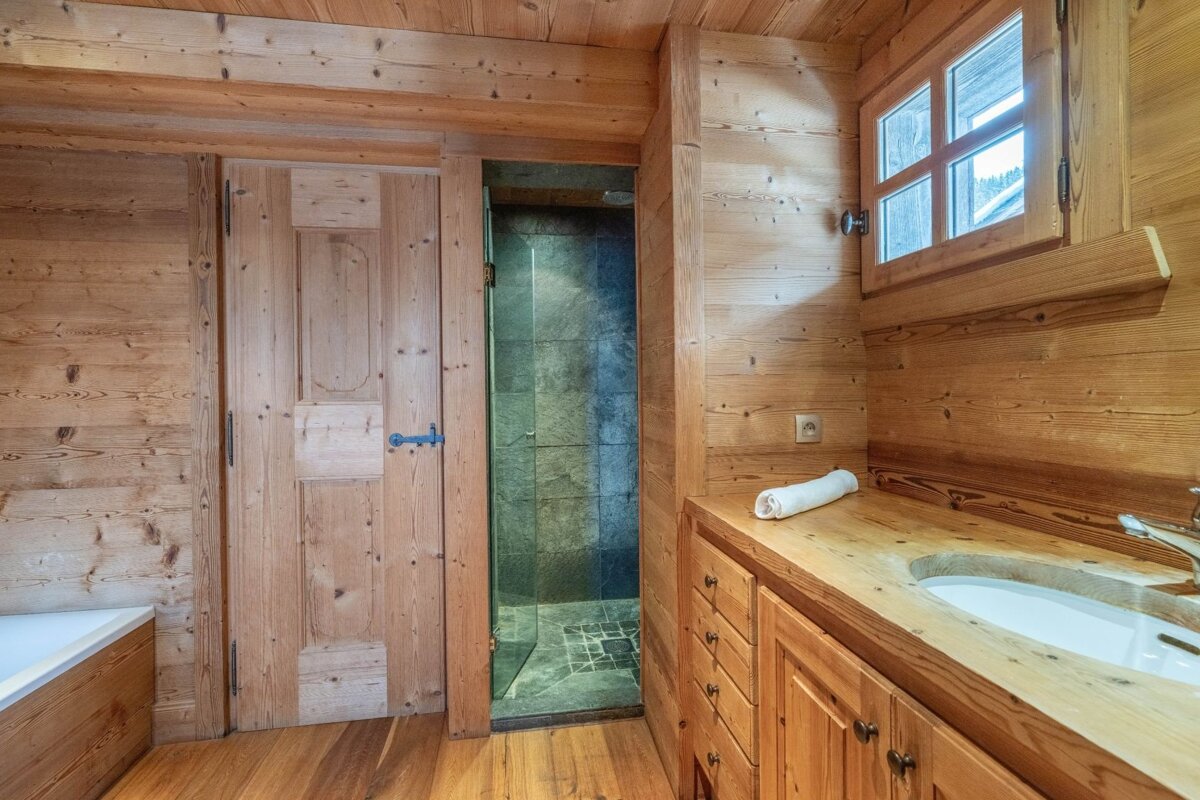 Rustic wood-paneled bathroom featuring a vanity sink, door, and a walk-in shower with dark grey tiles.