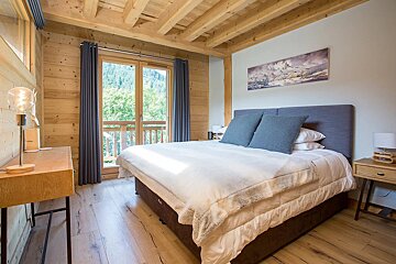 Cozy, modern bedroom with wood walls & ceiling, large bed, and a balcony offering a lush mountain view.