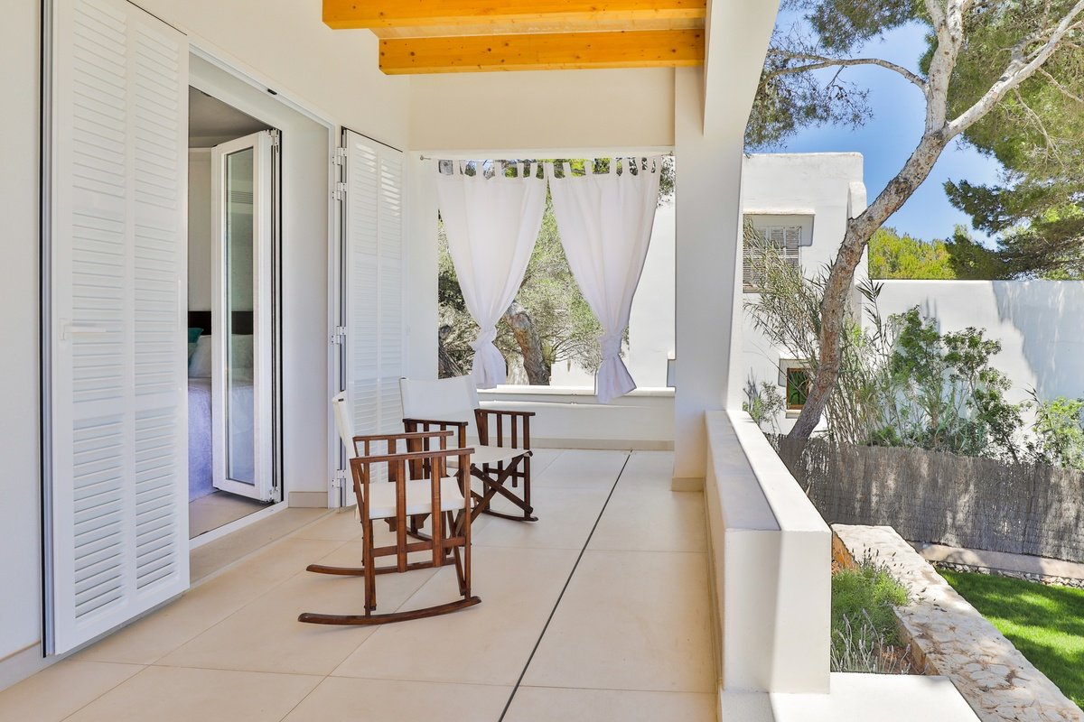 A balcony with two rocking chairs and white curtains