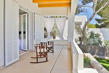 A balcony with two rocking chairs and white curtains