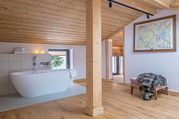 A modern, rustic attic bathroom features a freestanding tub, wood-paneled ceiling/floor, and a map. Cozy, natural light fills the space.
