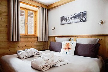 Cozy, rustic bedroom with wood paneling, a comfy bed with bathrobes and a fox pillow, mountain art, and a window with curtains.
