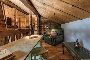 A green leather chair sits in an attic next to a desk