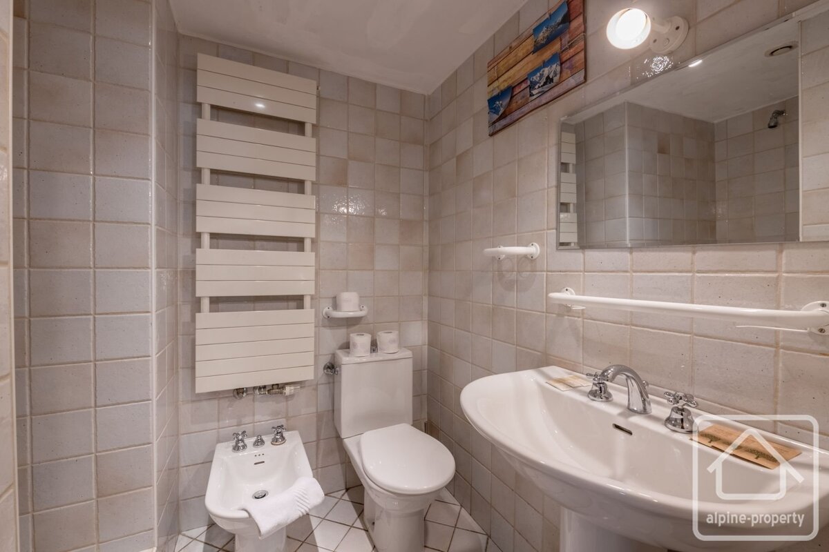 A tiled bathroom with a sink, toilet, bidet, towel warmer, and a mirror on the wall.