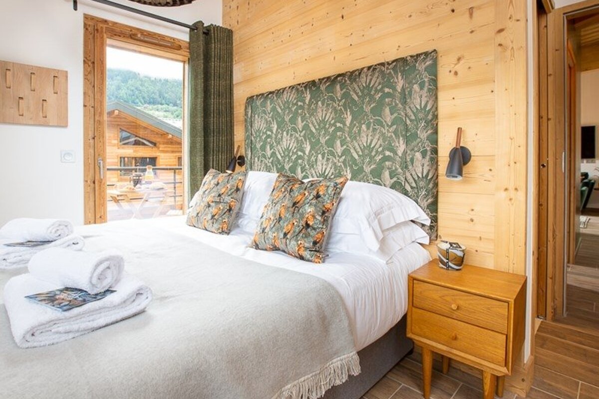 Cozy chalet bedroom with wood-paneled walls, a bed with a green patterned headboard, and glass doors leading to a balcony.