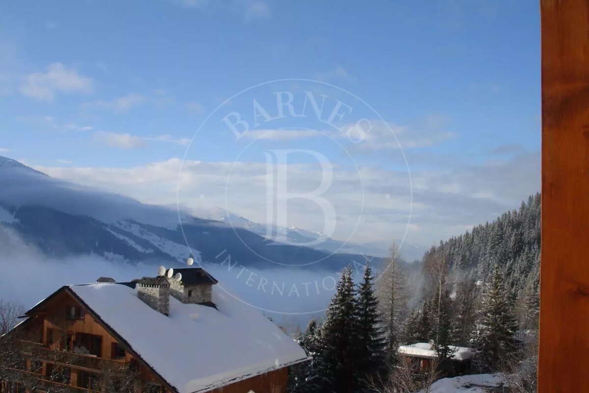 Snow-covered wooden chalets and pine trees in a misty mountain valley under a blue sky.