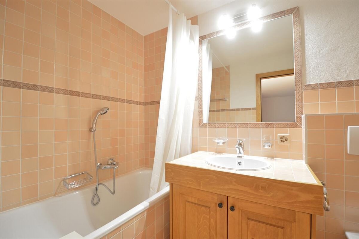 A bathroom with peach-colored tiles, a white bathtub and shower curtain, and a wooden vanity with a sink and mirror.