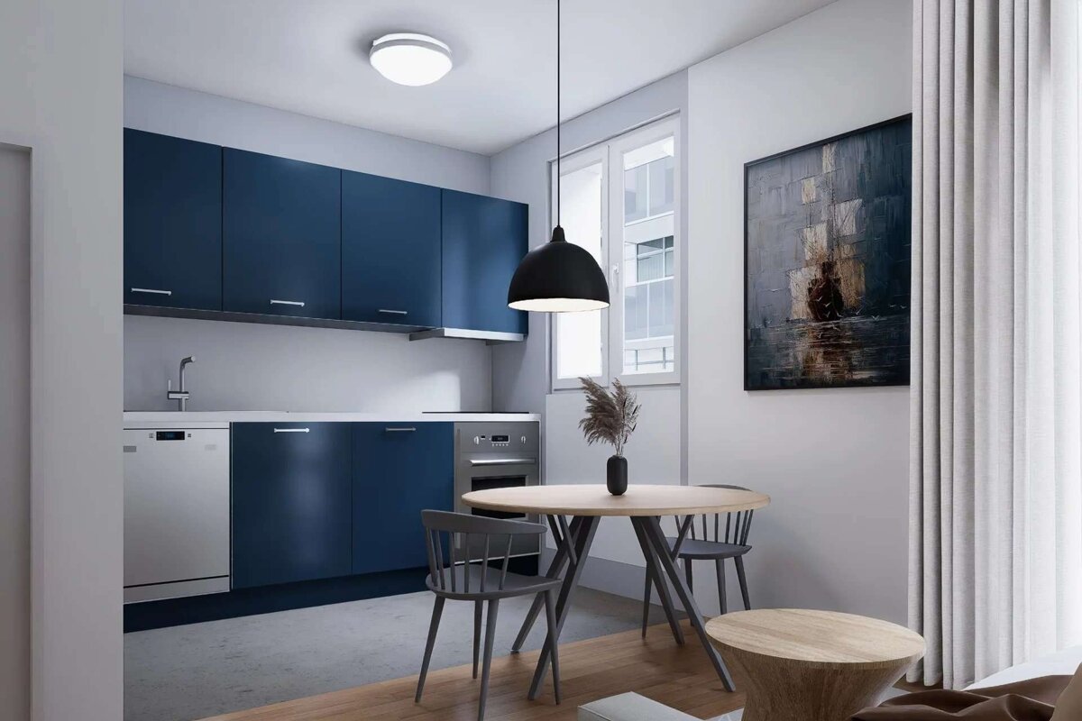 A modern kitchen and dining area with navy blue cabinets, white countertops, a round wooden table, grey chairs, and an abstract painting.