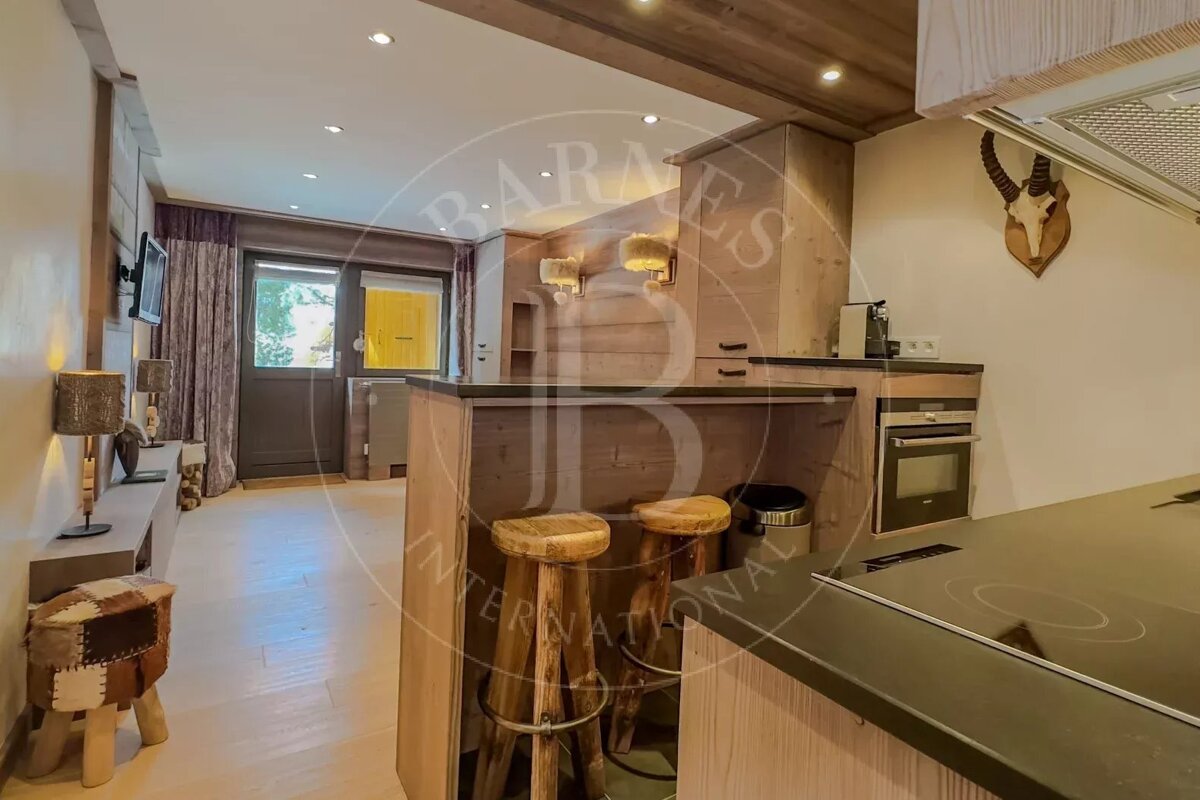 A cozy, rustic kitchen and living area with wooden accents, a bar counter with stools, modern appliances, and a wall-mounted deer skull trophy.