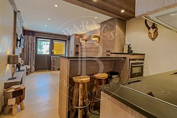 A cozy, rustic kitchen and living area with wooden accents, a bar counter with stools, modern appliances, and a wall-mounted deer skull trophy.