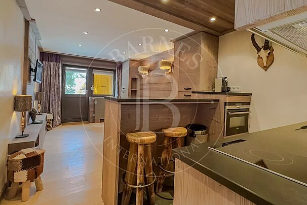 Modern rustic kitchen with wooden elements, a breakfast bar, stools, and warm lighting in a cozy apartment.