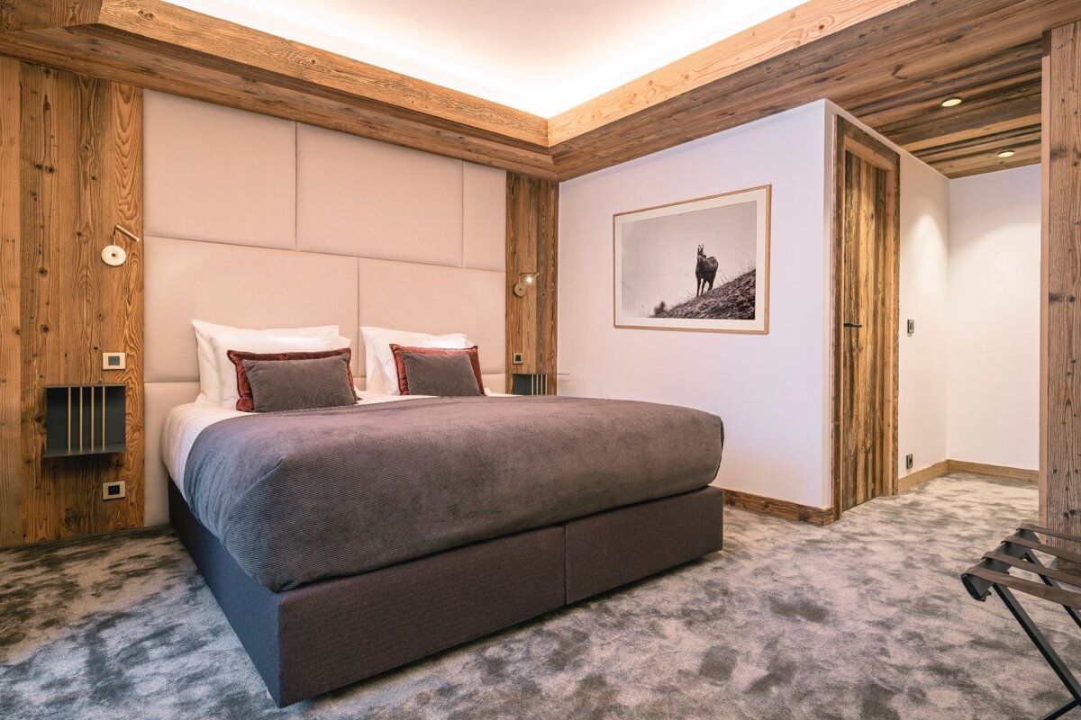Cozy bedroom with a large bed, plush grey bedding, warm wood paneling, a padded headboard, grey carpet, and a chamois picture.