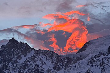 A mountain covered in snow with a red cloud in the sky