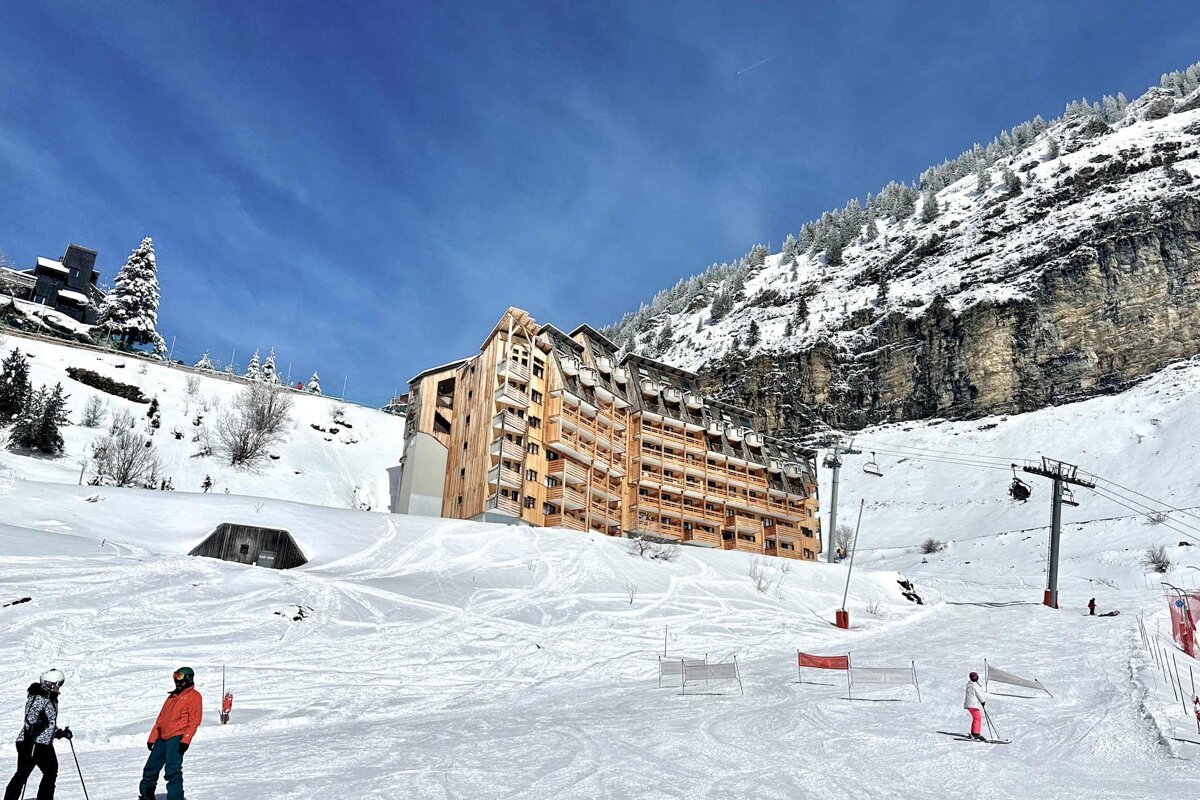 Skiers on a snowy slope with a large building in the background