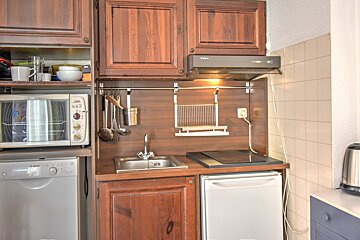 A compact, organized kitchen featuring dark wood cabinets, a sink, stove, microwave, dishwasher, and small fridge.