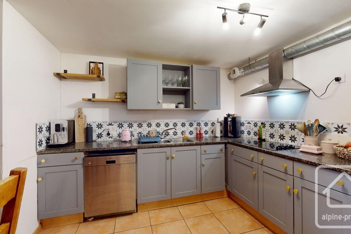 A modern kitchen features grey cabinets, patterned black & white backsplash, granite counters, stainless steel appliances, and tiled flooring.