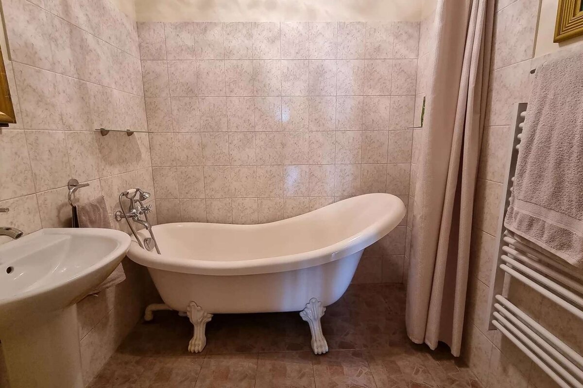 A traditional bathroom with a white clawfoot tub, pedestal sink, tiled walls, shower curtain, and a towel rack with a towel.