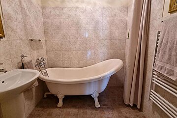 A traditional bathroom with a white clawfoot tub, pedestal sink, tiled walls, shower curtain, and a towel rack with a towel.