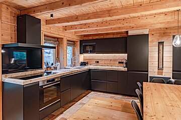 Modern matte black kitchen cabinets in a rustic log cabin with wooden walls and exposed ceiling beams.