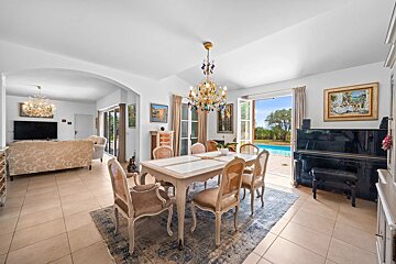 A bright dining room with elegant furniture, a piano, and doors opening to a pool, with a living room visible through an archway.