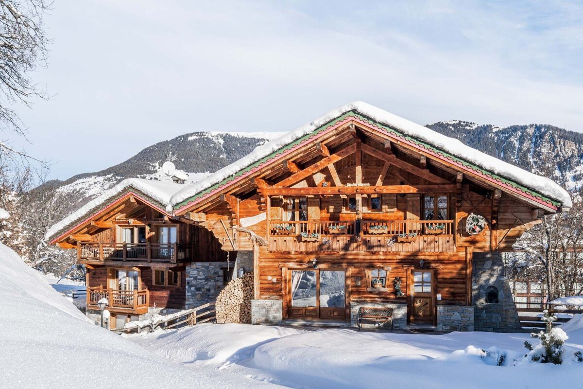 A beautiful wooden alpine chalet covered in snow, set against a stunning winter mountain landscape.