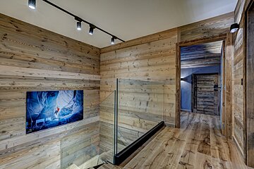 A wooden hallway with a glass railing and a painting on the wall